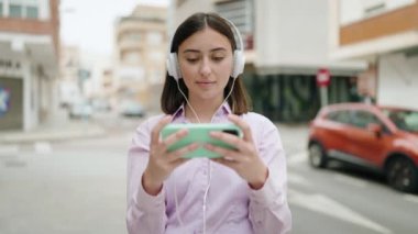 Young hispanic woman smiling confident playing video game at street