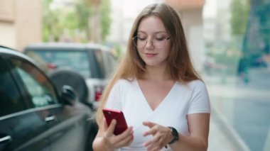 Young blonde woman smiling confident making selfie by the smartphone at street