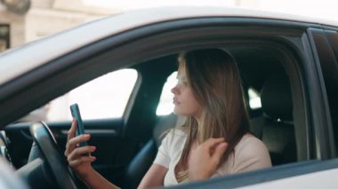Young woman using smartphone sitting on car at street