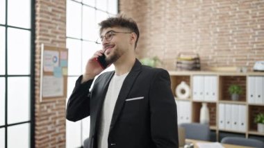 Genç Arap iş adamı gülümseyerek ofisteki akıllı telefondan konuşuyor.