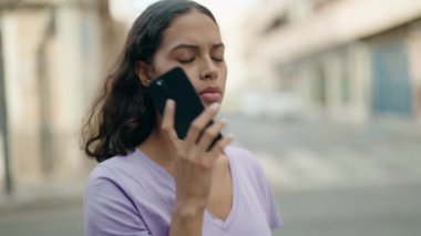 Genç Afro-Amerikalı kadın sokakta endişeli bir ifadeyle akıllı telefondan konuşuyor.