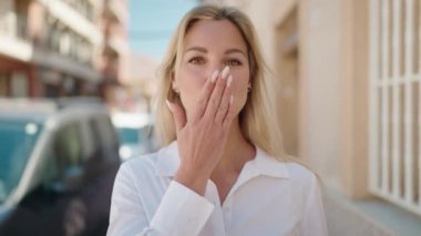 Genç sarışın kadın gülümsüyor. Kendine güveniyor. Öpüşme hareketi yapıyor.