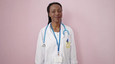 Afro-Amerikalı kadın doktor, pembe arka planda kendine güvenen gülümsüyor.