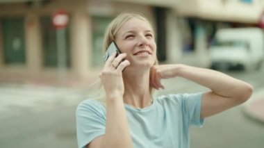 Genç sarışın kadın gülümsüyor. Kendine güveni tam. Akıllı telefondan konuşuyor.