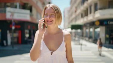 Young blonde woman talking on the smartphone walking at street