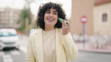 Young woman smiling confident listening audio message by the smartphone at street