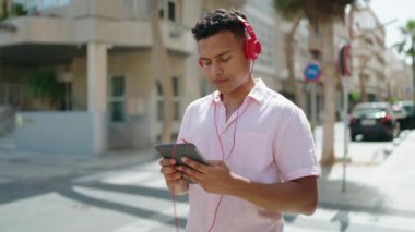 Young latin man using touchpad and headphones at street