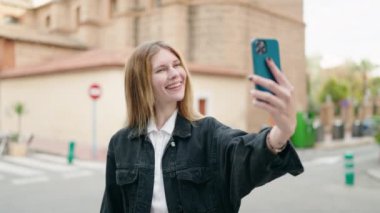 Beyaz bir kadın sokakta akıllı telefon kullanarak gülümsüyor.