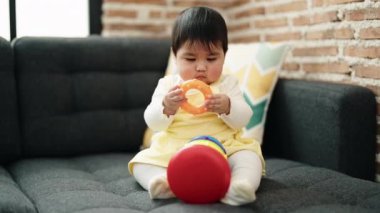 Adorable hispanic baby playing with hoops sitting on sofa at home