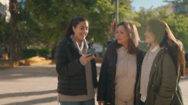 Anne ve kızları gülümsüyor. Parktaki akıllı telefondan özçekim yapıyorlar.