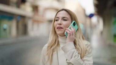 Genç sarışın kadın gülümsüyor. Kendine güveni tam. Akıllı telefondan konuşuyor.
