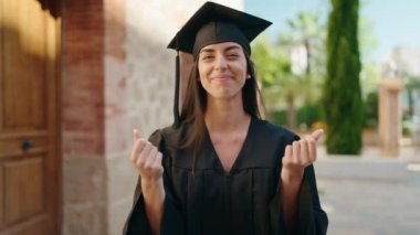 Mezuniyet üniforması giyen genç İspanyol kadın üniversitede el kol hareketi yaparak para harcıyor.
