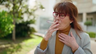 Orta yaşlı kadın yönetici sigara içiyor ve parkta öksürüyor.