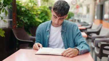 Kahve dükkanının terasında kitap okuyan genç bir İspanyol.