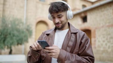 Genç Arap adam kendinden emin bir şekilde gülümsüyor müzik dinliyor ve sokakta dans ediyor.