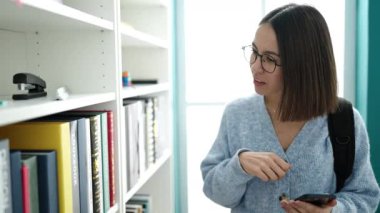 Kütüphane Üniversitesi 'nde akıllı telefondan kitap arayan güzel İspanyol bir kız öğrenci.