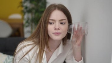 Sarışın genç bir kadın sokakta camları olan komşuları gözetliyor.