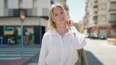 Genç sarışın kadın gülümsüyor. Elinde ceket tutuyor.