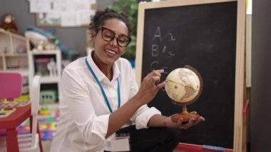 African american woman teacher smiling confident holding earth at kindergarten