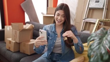 Genç, güzel, İspanyol bir kadın yeni evinde elinde anahtarlarla görüntülü arama yapıyor.