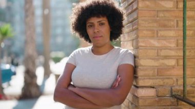 Genç Afrikalı Amerikalı kadın gülümsüyor. Kendine güveni tam. Sokakta kollarını kavuşturmuş duruyor.