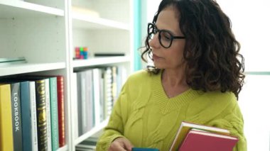 Orta yaşlı İspanyol kadın öğretmen kütüphanede akıllı telefon rehberi kullanıyor.