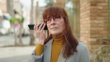 Orta yaşlı kadın işletme yöneticisi sokakta sesli mesaj dinliyor