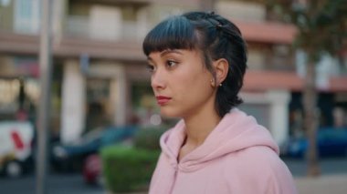 Young hispanic woman standing with serious expression at street