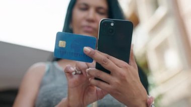 Orta yaşlı İspanyol kadın akıllı telefon ve kredi kartı kullanıyor.