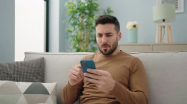 Genç İspanyol adam evde akıllı telefon kullanıyor.