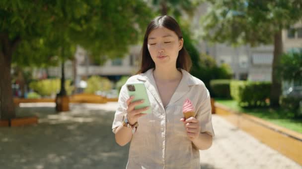 Chińska Kobieta Pomocą Smartfona Jedząc Lody Spacerując Parku — Wideo stockowe