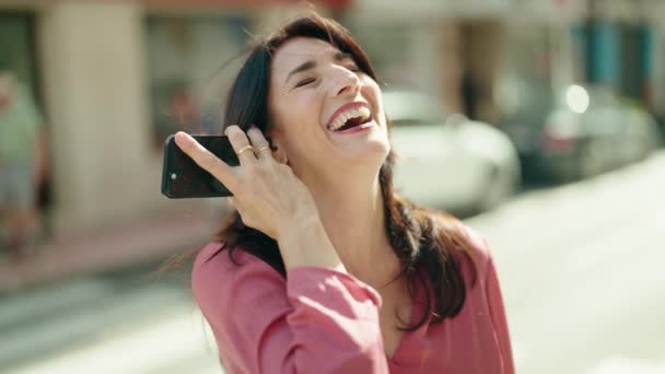 中世のヒスパニック女性笑顔自信に満ちたリスニング音声メッセージによってスマートフォンでストリート — ストック動画