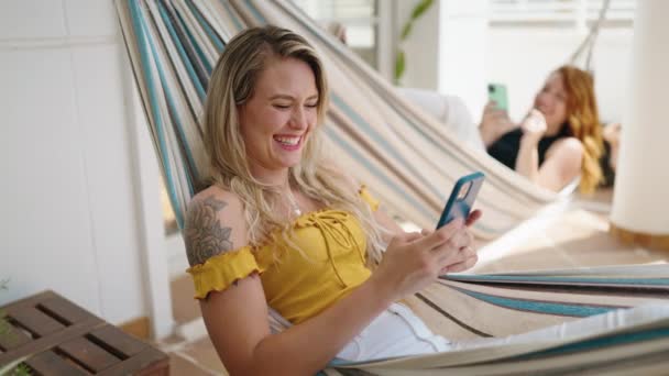 Two Women Using Smartphones Lying Hammock Home Terrace — Video Stock