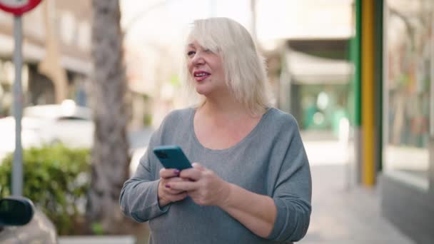 Μέση Ηλικία Ξανθιά Γυναίκα Χαμογελά Αυτοπεποίθηση Χρησιμοποιώντας Smartphone Στο Δρόμο — Αρχείο Βίντεο