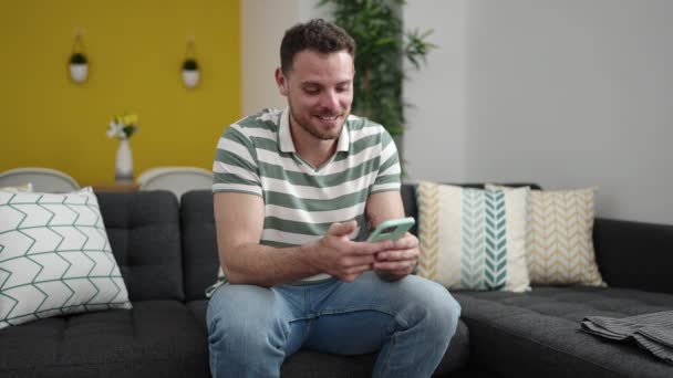 Young Caucasian Man Smiling Using Smartphone Sitting Sofa Home — Vídeos de Stock