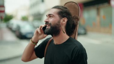 Young hispanic man musician talking on smartphone holding guitar case at street