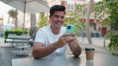 Genç İspanyol adam kahve dükkanının terasında akıllı telefon kullanarak kutlama yapıyor.