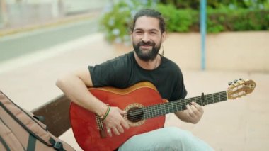 Genç İspanyol müzisyen klasik gitar çalıyor. Parkta bankta oturuyor.