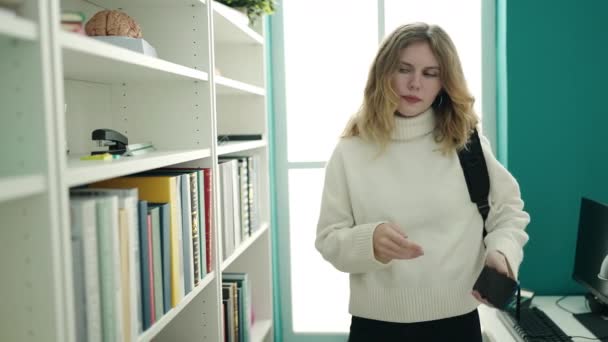 年轻的金发女学生拿着图书馆大学的书架 — 图库视频影像