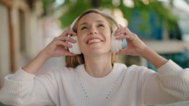 Young blonde woman listening to music and dancing at street