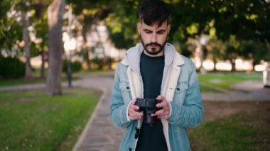 Young hispanic man standing with serious expression using camera at park