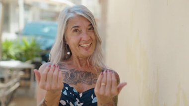 Orta yaşlı, gri saçlı, gülümseyen, kendine güveni tam bir kadın.