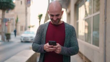 Sokakta akıllı telefon kullanarak kendine güvenen genç kel adam.