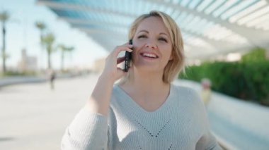 Akıllı telefondan konuşan genç sarışın kadın parkta nöbet tutuyor.