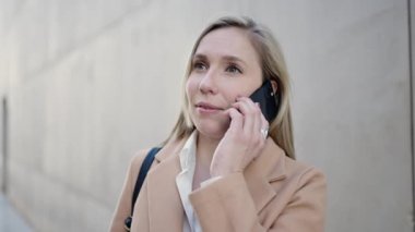 Genç sarışın kadın gülümsüyor. Kendine güveni tam. Akıllı telefondan konuşuyor.