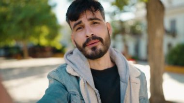 Genç İspanyol adam gülümsüyor. Parkta kendine güvenen bir video çağrısı var.