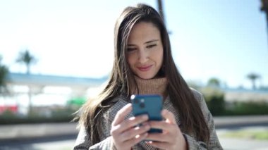 Güzel İspanyol kadın sokakta akıllı telefon kullanarak gülümsüyor.