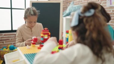 Group of kids playing with construction blocks sitting on table at kindergarten