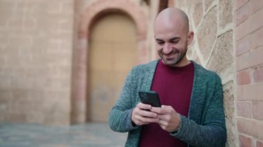 Sokakta akıllı telefon kullanarak kendine güvenen genç kel adam.