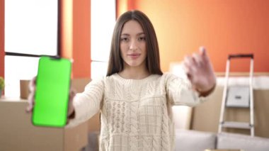 Young beautiful hispanic woman smiling confident holding key showing screen smartpho at new home